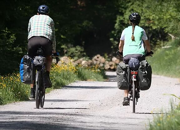 Ein Mann und eine Frau fahren mit dem Fahrrad einen Waldweg entlang.