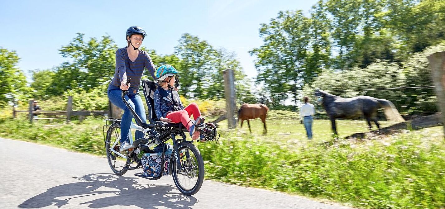 Unterwegs mit dem Pino von Hase Bikes. Frau und Kind fahren auf einen Tandem Rad und an einer Pferdewiese vorbei